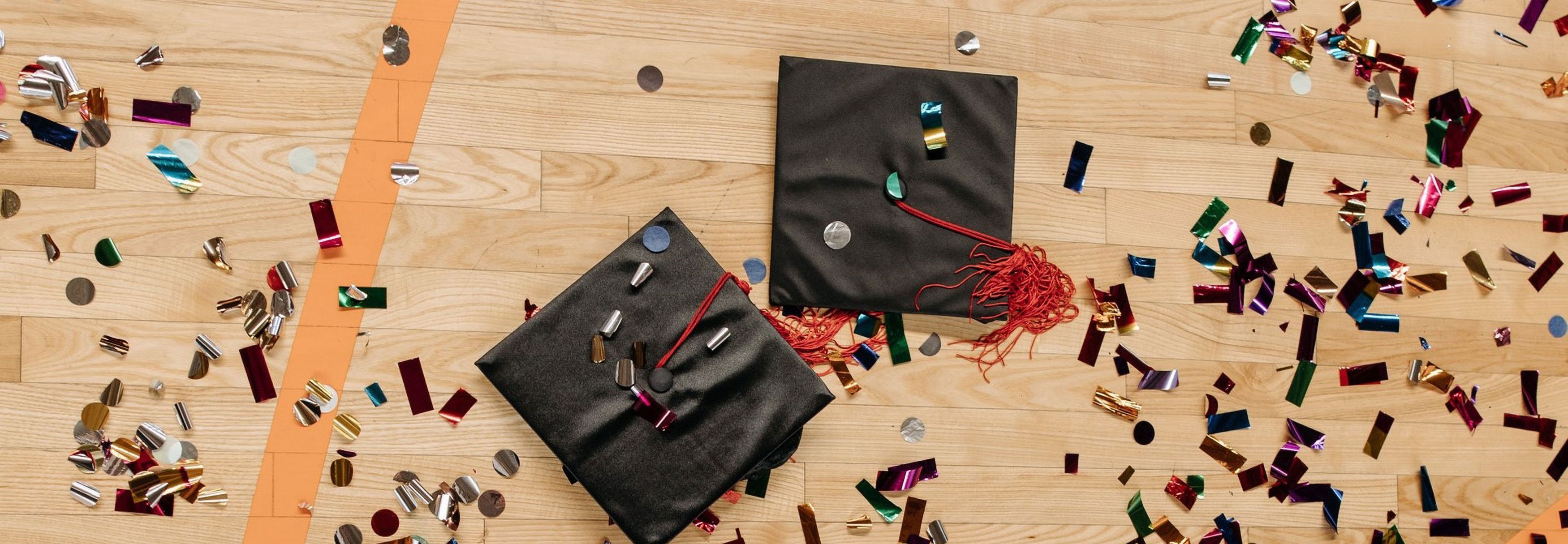 Two graduation caps on a gym floor with some confetti. It's a stock photo. I'll replace it with a picture of the graduating class this year.