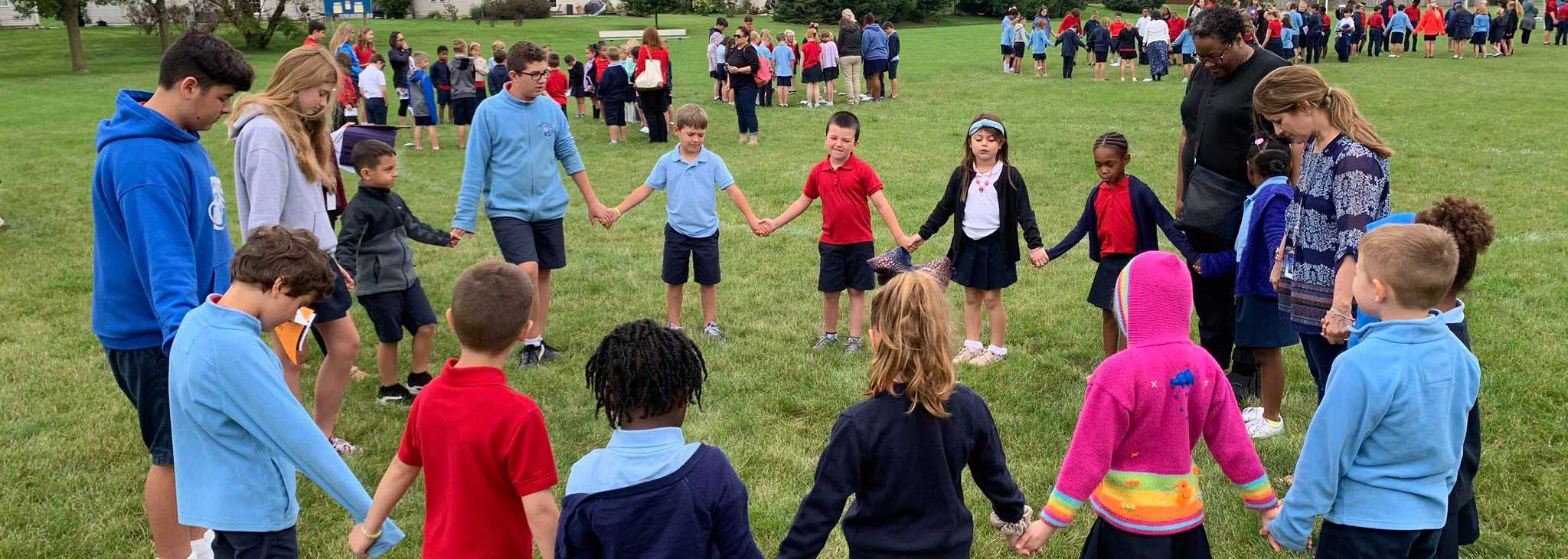 students of all ages holding hands in a circle praying outside